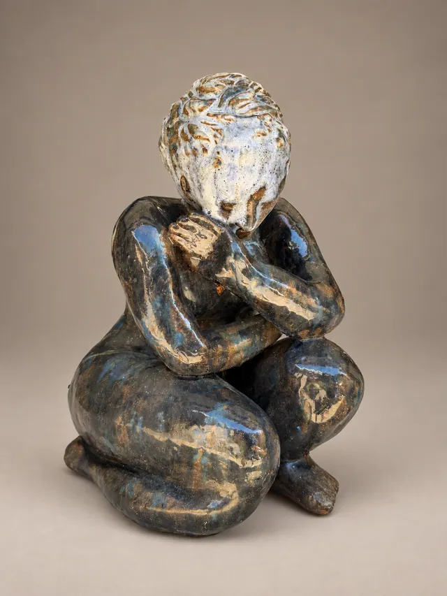 Crouching figure with hands to face, glazed in blue and brown
