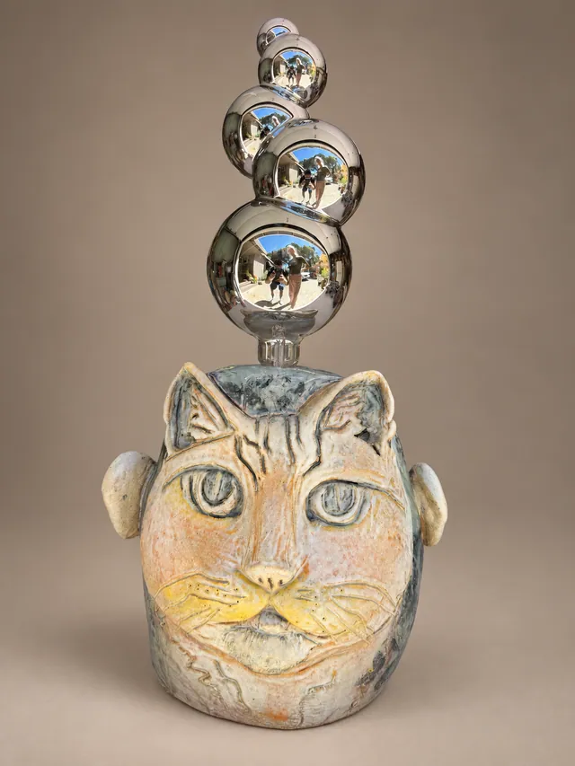 Two-sided head, a cat on one side and a man in glasses on the other, topped with chrome spheres