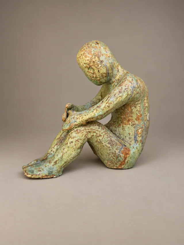 Seated figure hugging its knees, mottled green glaze