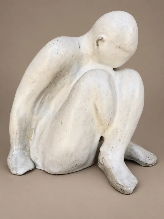 Smooth white seated figure with its head resting on its knees